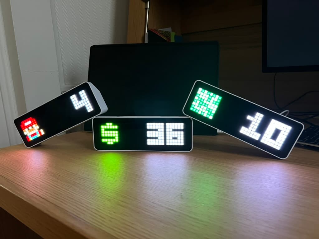 Three digital pixel displays arranged on a desk with live metrics